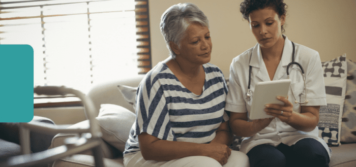 Health care worker reviewing information on a tablet with an older adult in a home setting.