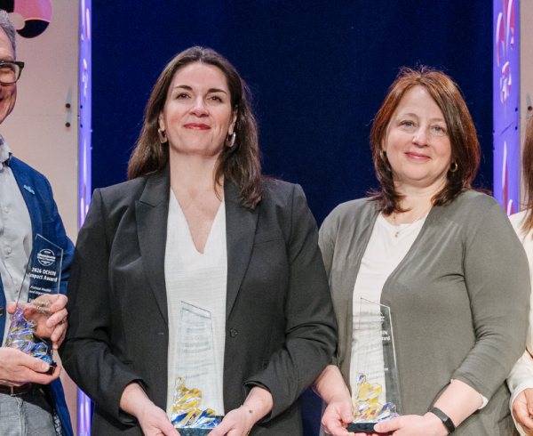 Four award recipients stand on stage holding glass trophies at the 2026 OCHIN Learning Forum Impact Awards in New Orleans, with event lighting and decorative backdrop behind them.