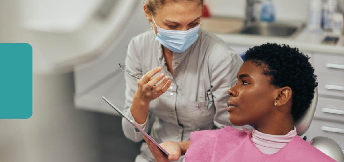 dentist consults with a patient in a dental exam room while reviewing care information on a clipboard.