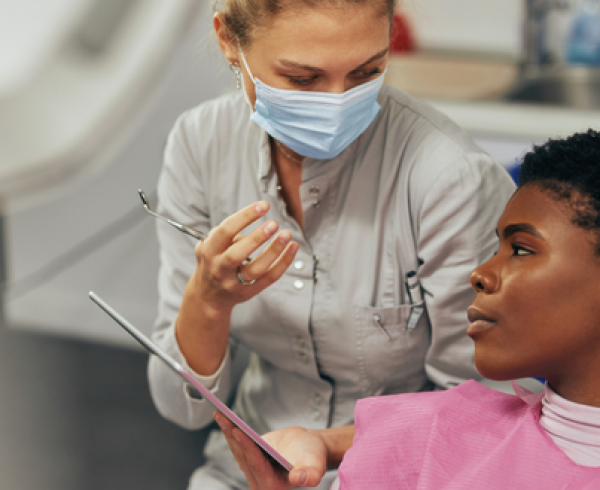 dentist consults with a patient in a dental exam room while reviewing care information on a clipboard.