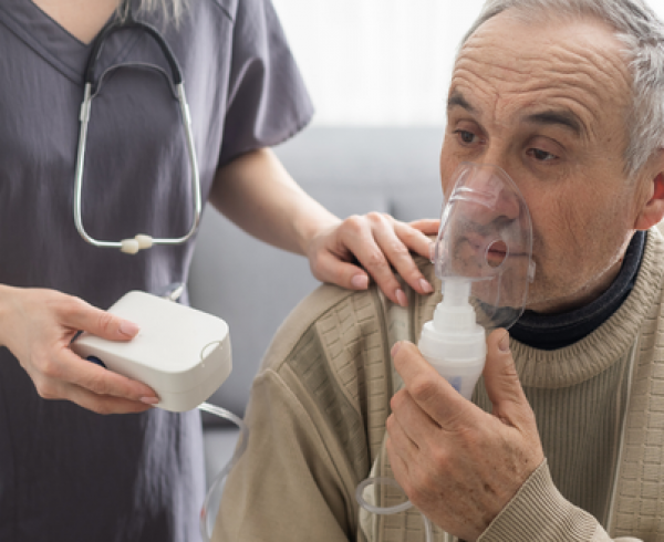 A patient uses a nebulizer mask while receiving support from a health care team member during a clinic visit.