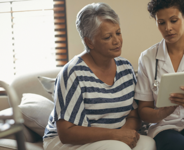 Health care worker reviewing information on a tablet with an older adult in a home setting.